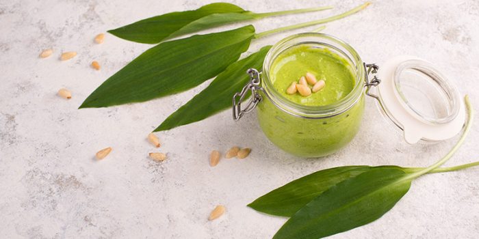 Pesto made from wild garlic, pine nuts and feta cheese in a glass, with fresh leaves on a white textured background, empty space for text